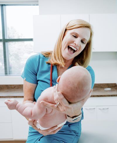 Smiling healthcare worker holding a baby in a bright clinic kitchen area