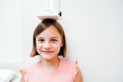 Young girl in a pink shirt balancing a bowl on her head, smiling against a white background