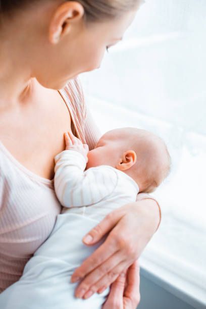 Parent holding and breastfeeding a baby near a bright window