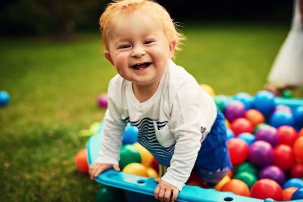 Smiling toddler playing in a colorful ball pit outdoors on green grass