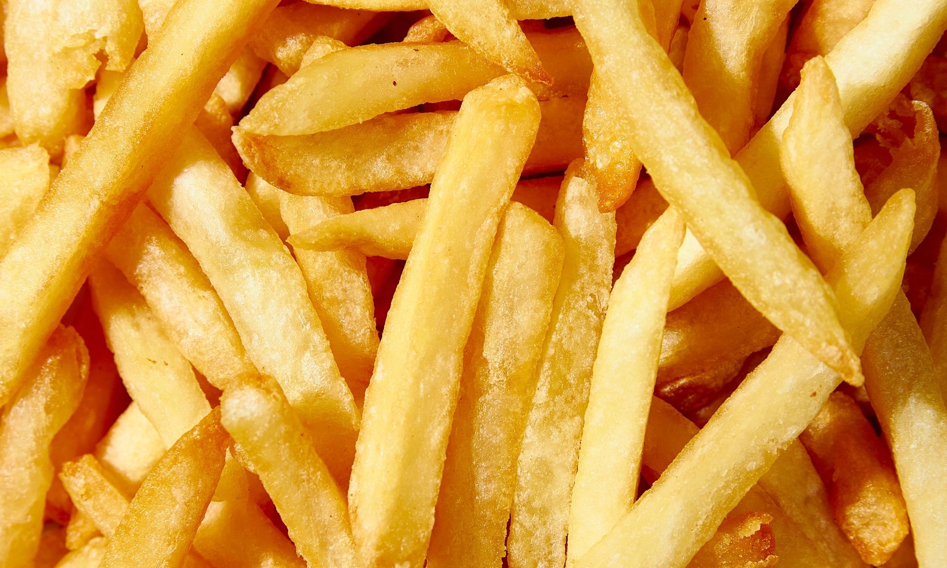 Nahaufnahme von goldbraunen Pommes Frites, die sich überlappen und den Rahmen ausfüllen.