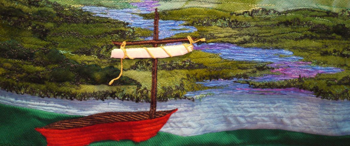Small red sailboat with a cream sail on blue water near a green shoreline