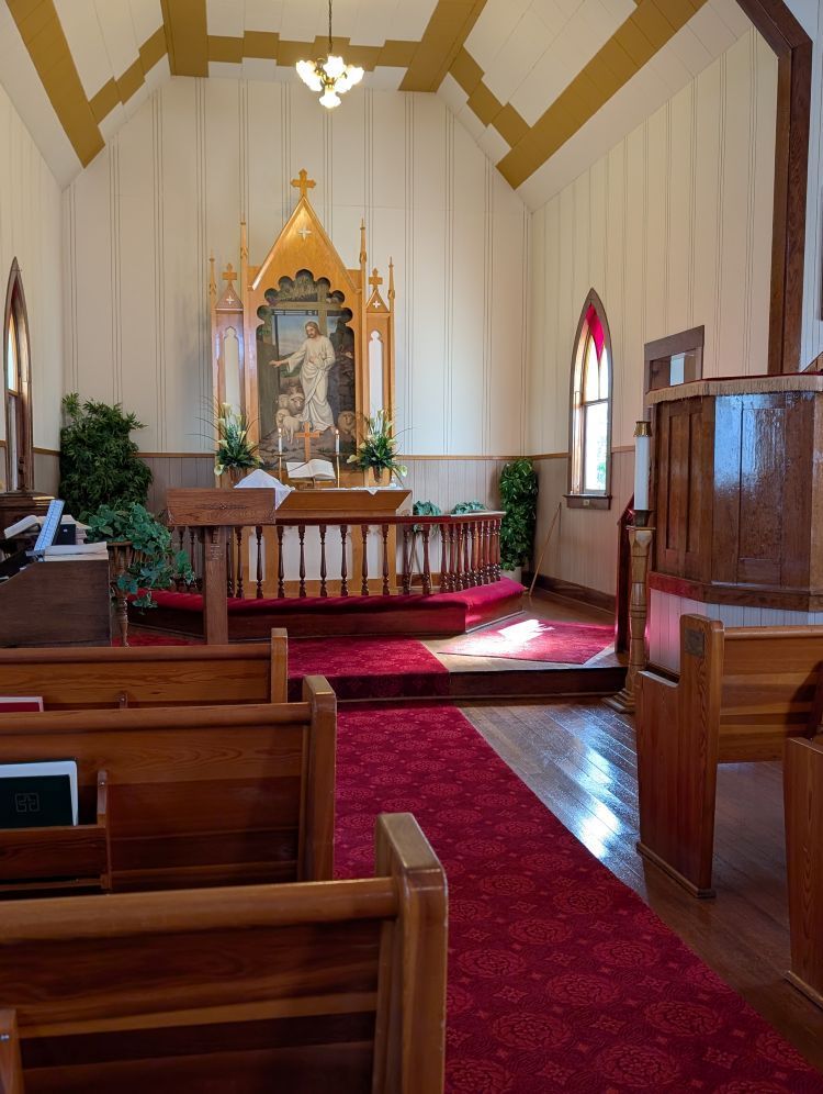 Small church sanctuary with red carpet, wooden pews, and altar with candles and flowers