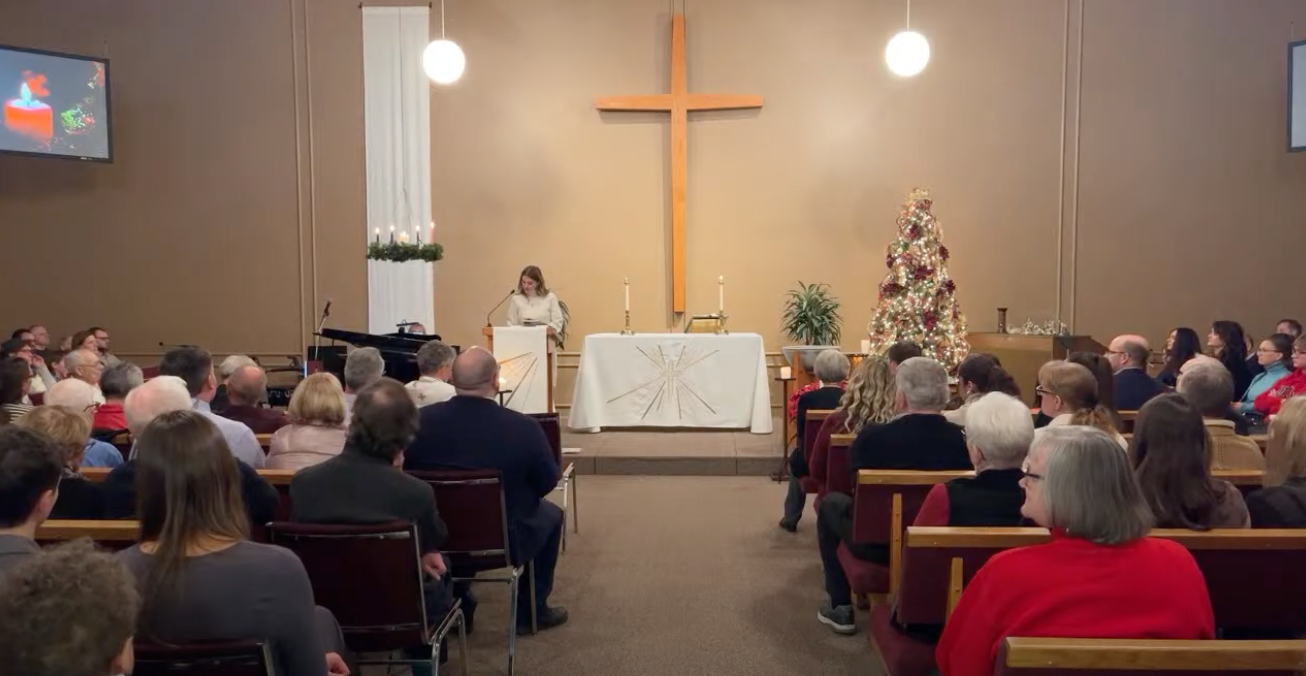 Church service with congregation seated facing an altar, cross, and lit Christmas tree