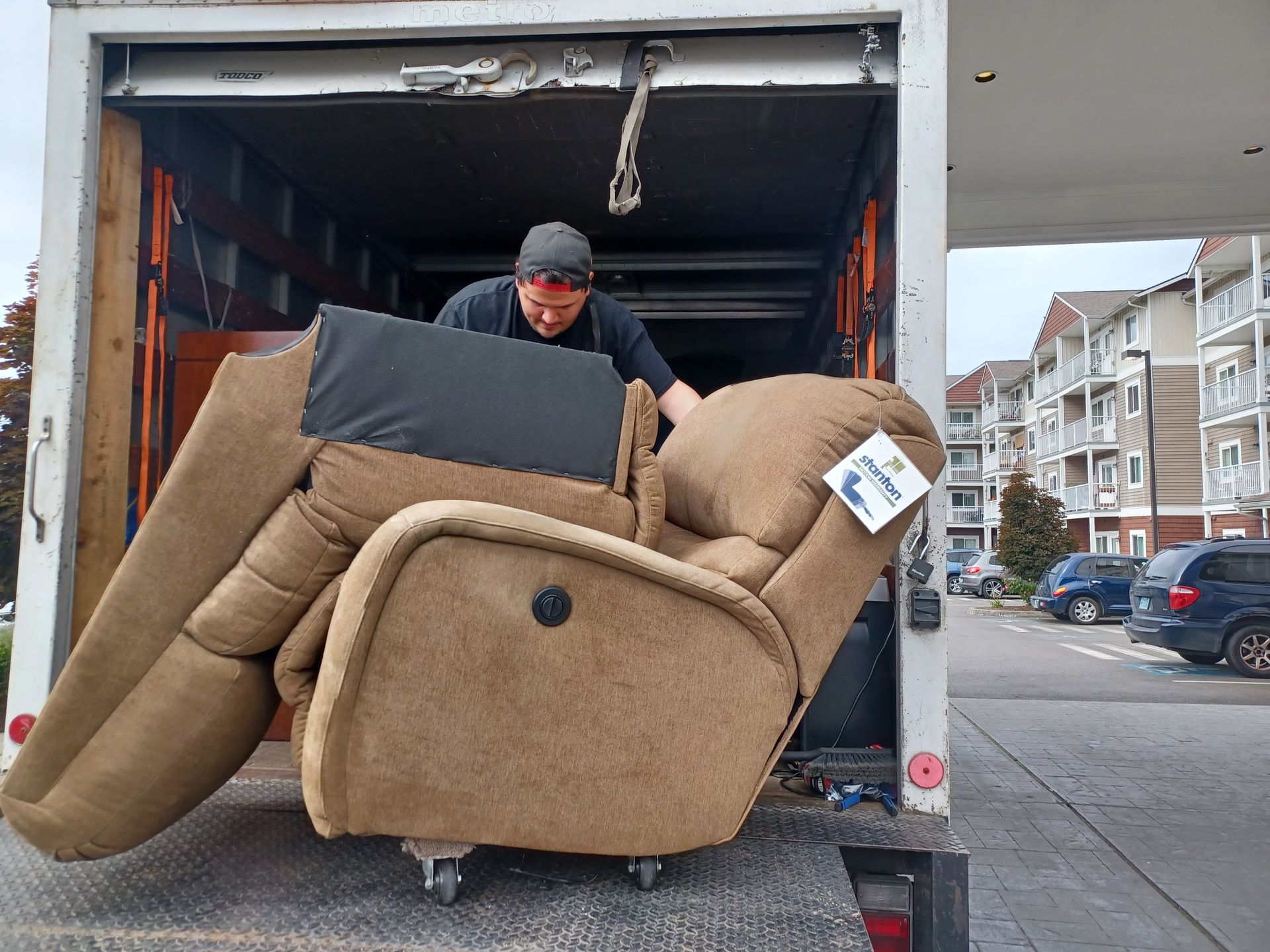 A person in a moving truck maneuvers a tan recliner on a small dolly.