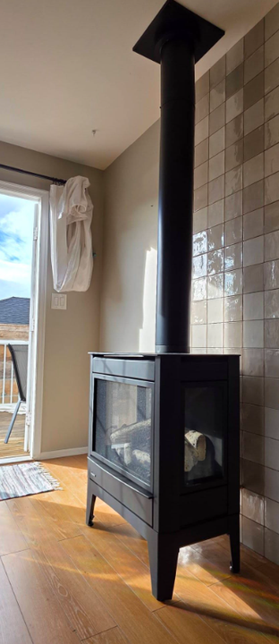Freestanding black gas stove with tiled wall and flue