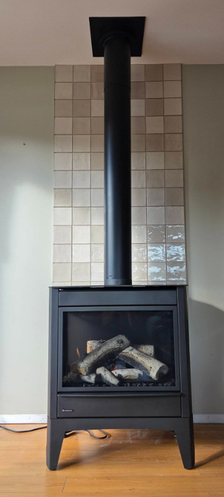Black gas fireplace with ceramic logs and tiled chimney wall