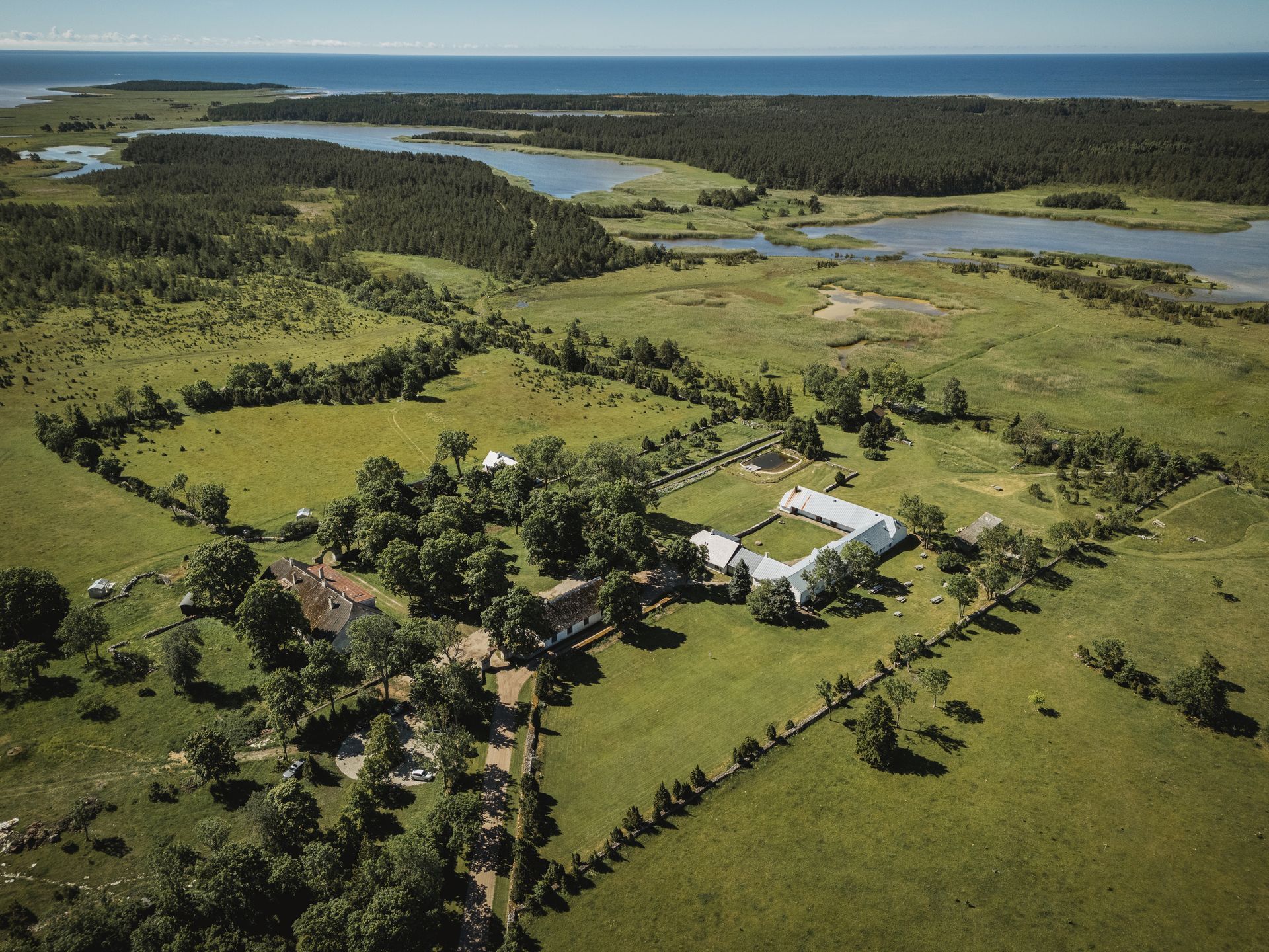 Aerial view of a white building complex surrounded by green fields, near a forest and the ocean.
