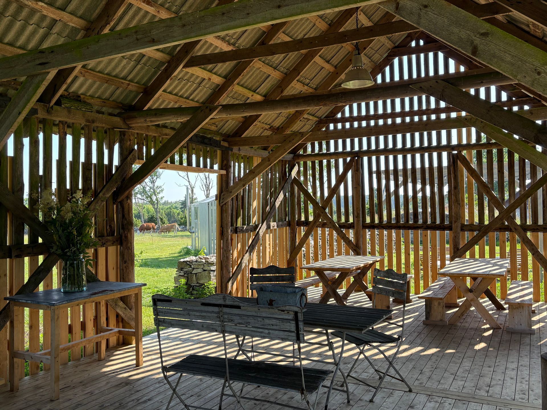 Rustic wooden shelter with tables and chairs, open to a sunny outdoor space.