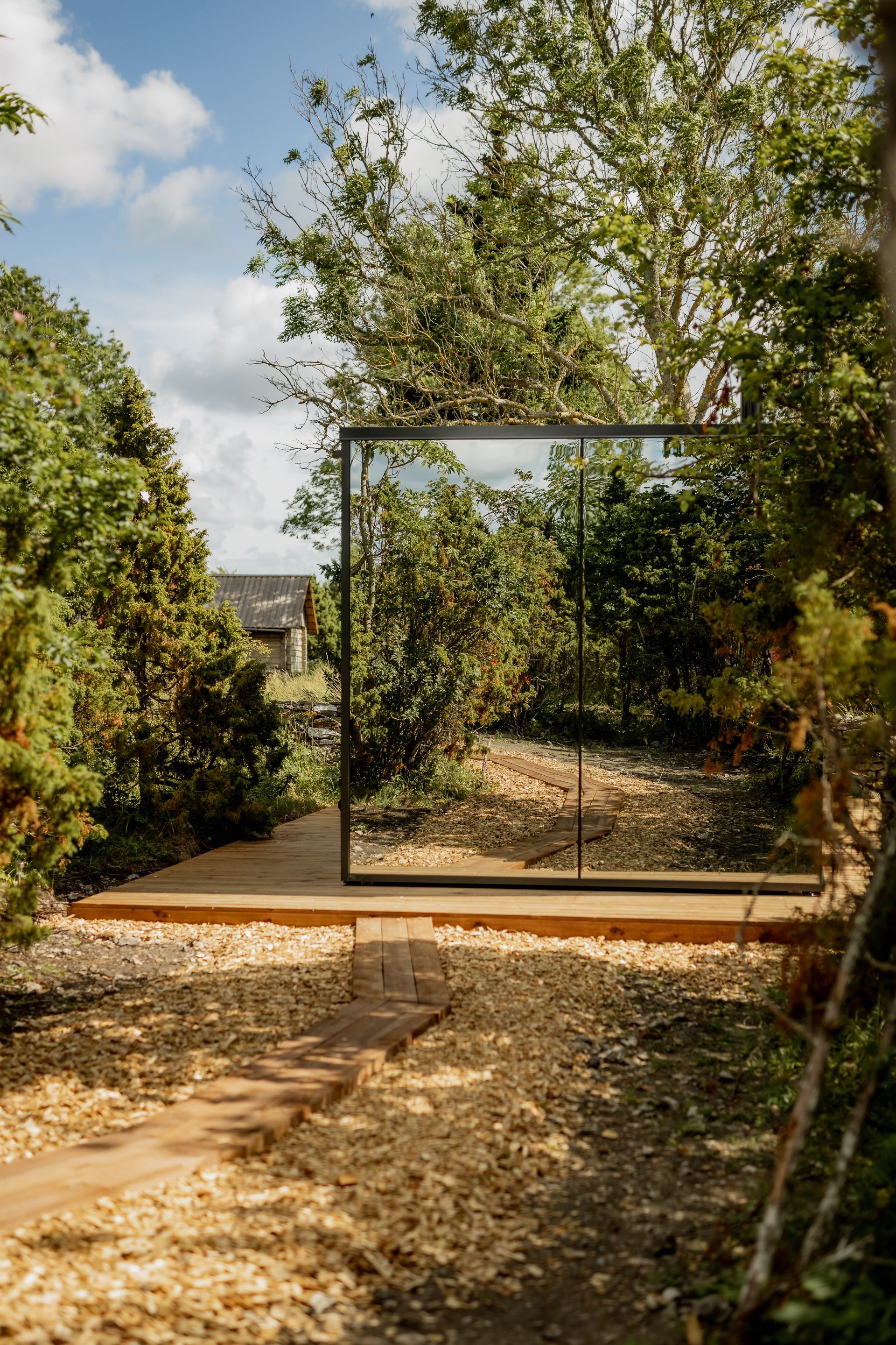 A large, framed mirror reflects trees and sky within a lush garden.