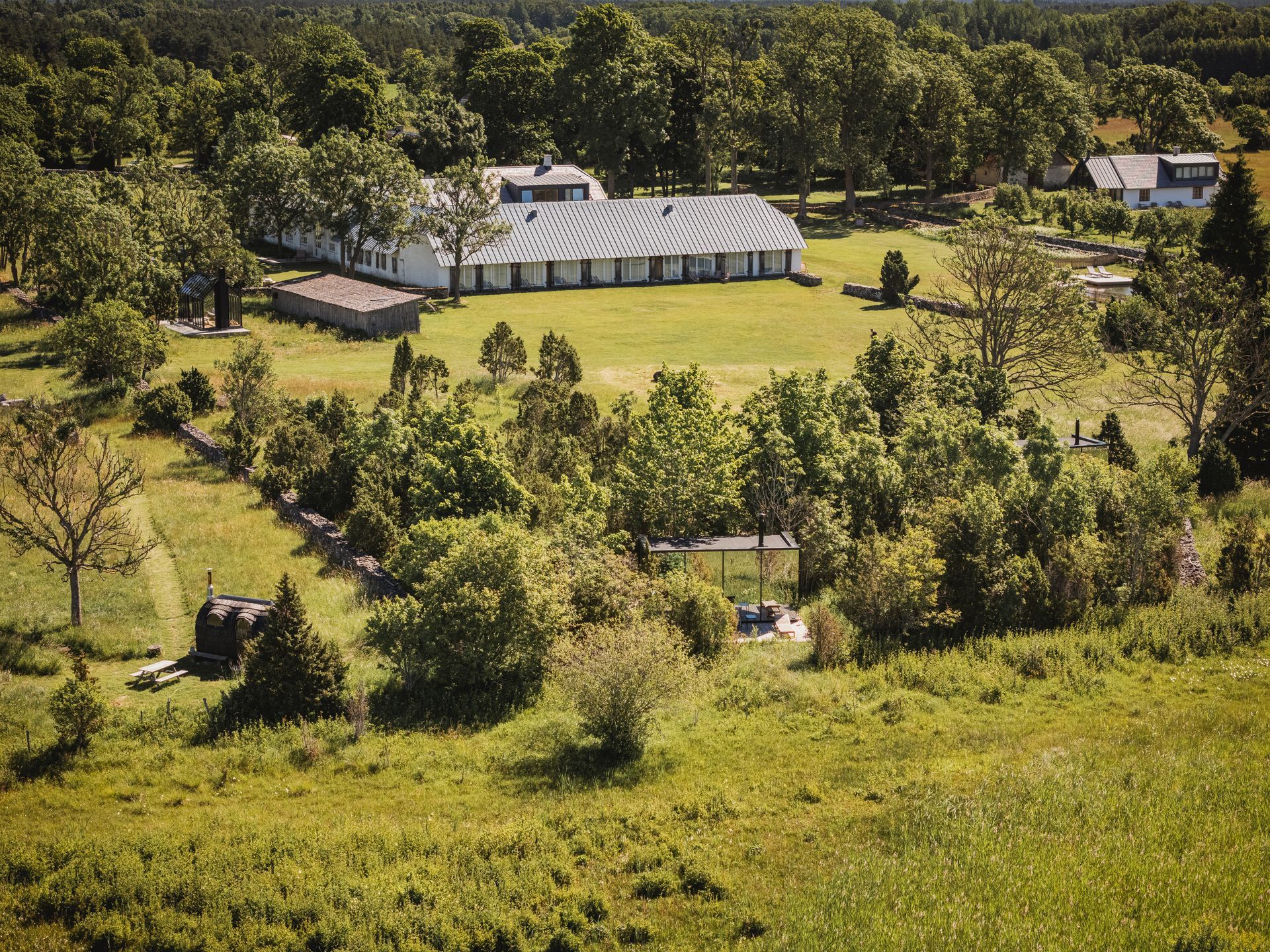 Aerial view of a white, multi-room building on a green lawn surrounded by trees and fields.