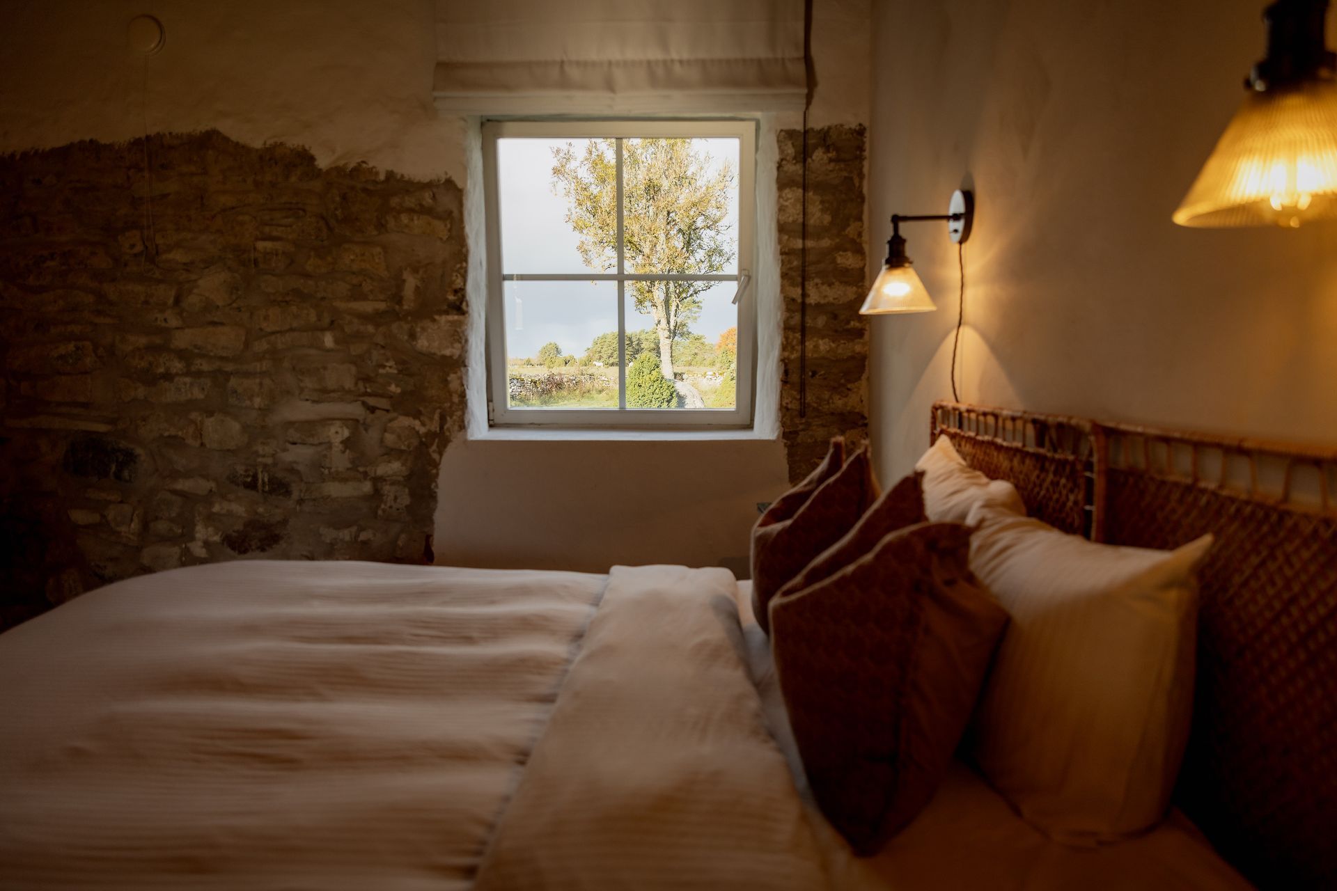 Bedroom with a bed, stone wall, window, and two wall sconces casting a warm glow.