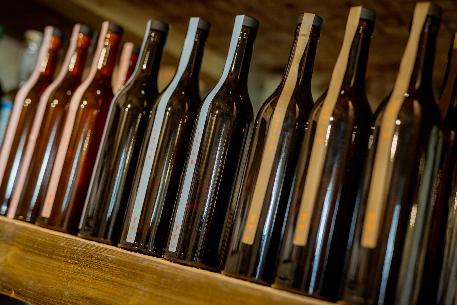 Row of wine bottles on a wooden shelf, varying shades of brown.