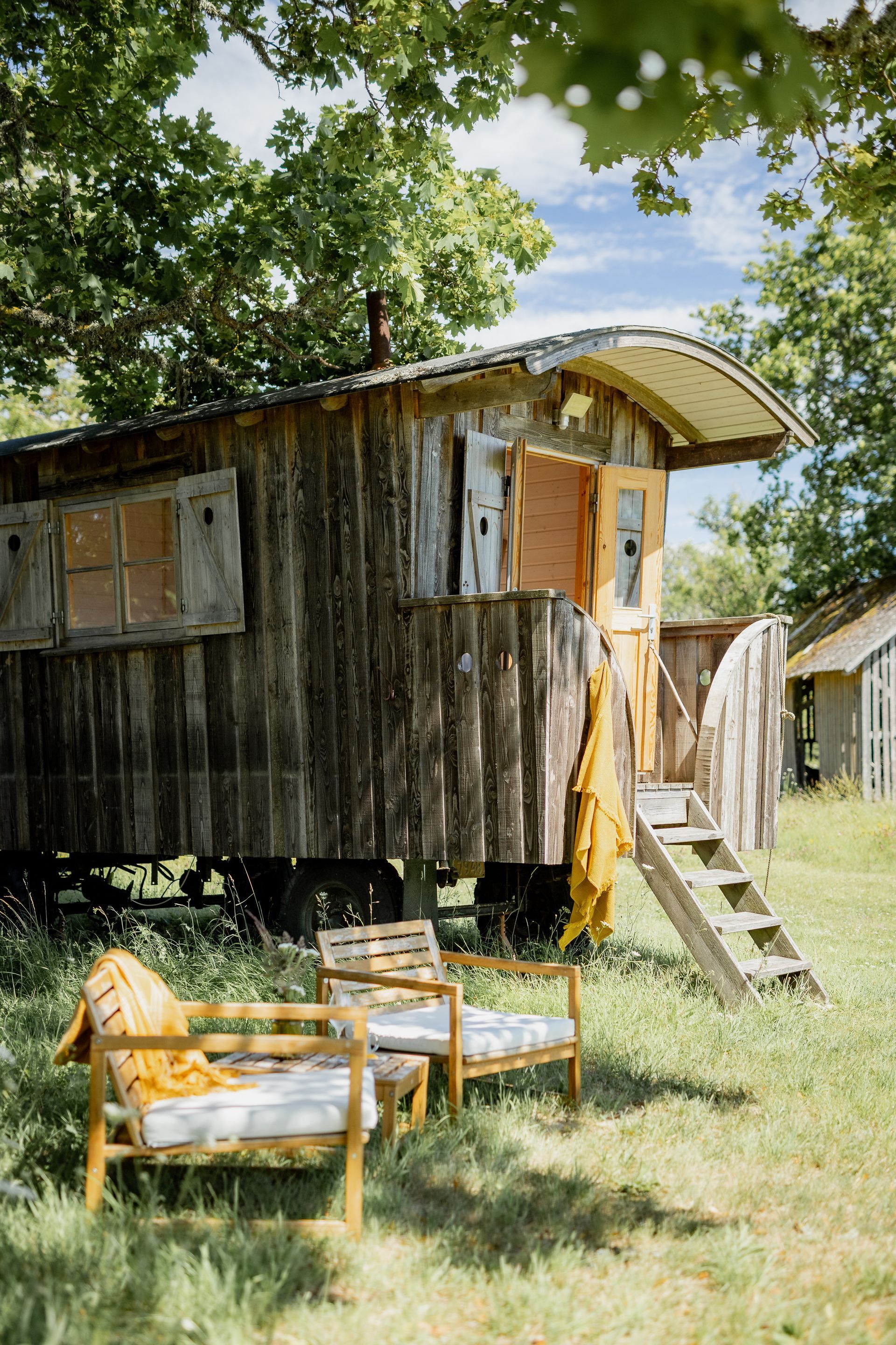 Rustic wooden wagon-like structure with chairs on a grassy lawn. Yellow blankets and sunlight add warmth.