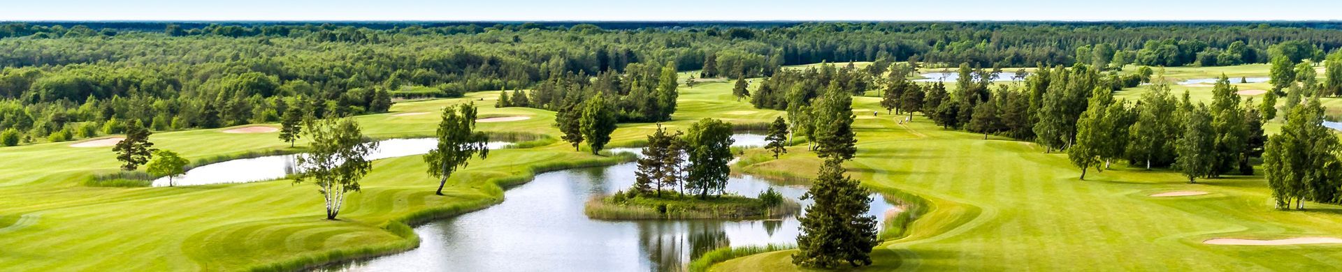 A green golf course with a lake and trees.