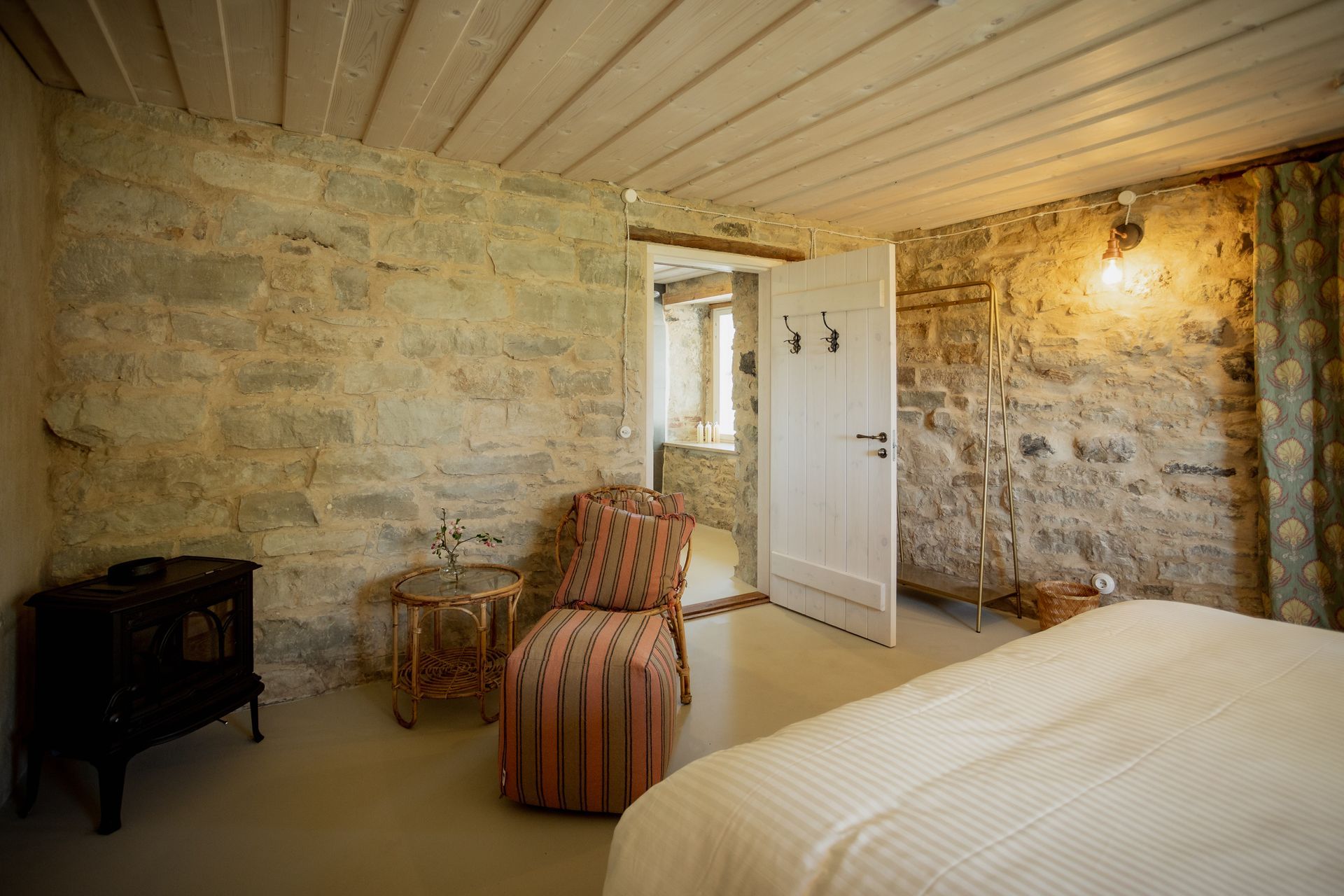 Bedroom with stone walls, white door, patterned chair, and bed.