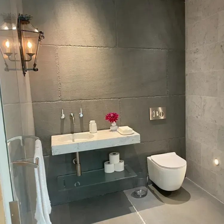 Modern gray bathroom with wall-mounted sink, toilet, lantern sconce, and towel rack