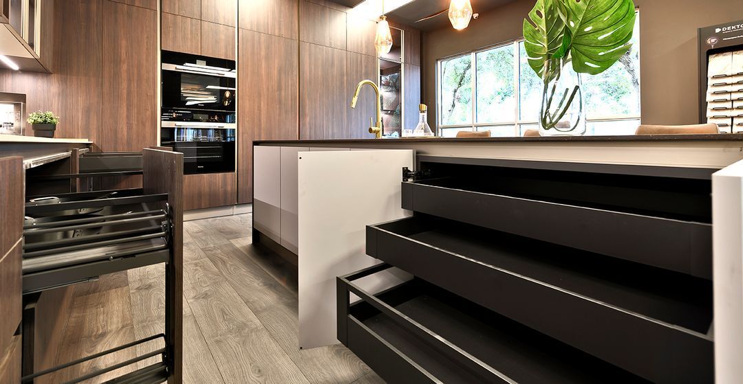 Modern kitchen with wood cabinets, black appliances, white island, and a large window over the sink