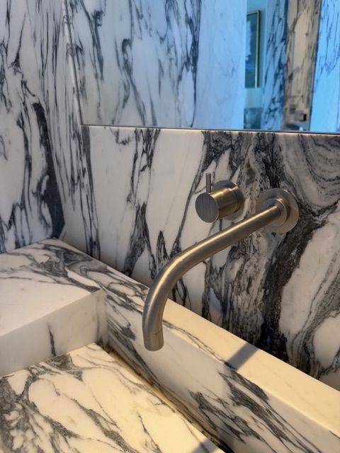 Marble bathroom sink with curved chrome faucet and veined white-and-gray stone walls