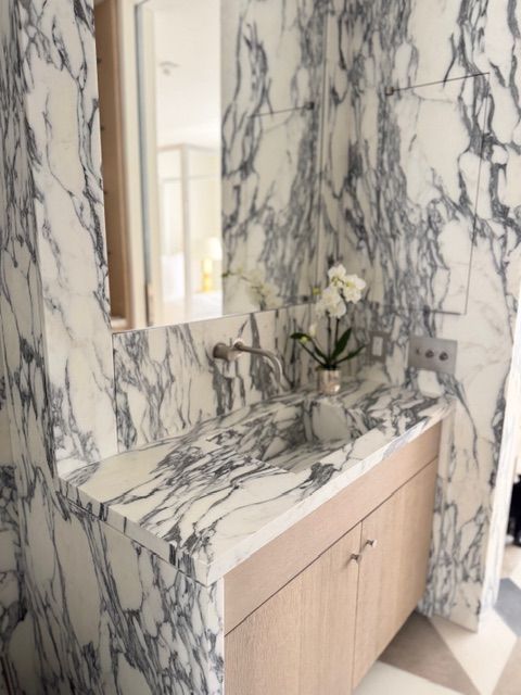 Marble-tiled bathroom vanity with wood cabinets, mirror, and white flowers in a vase