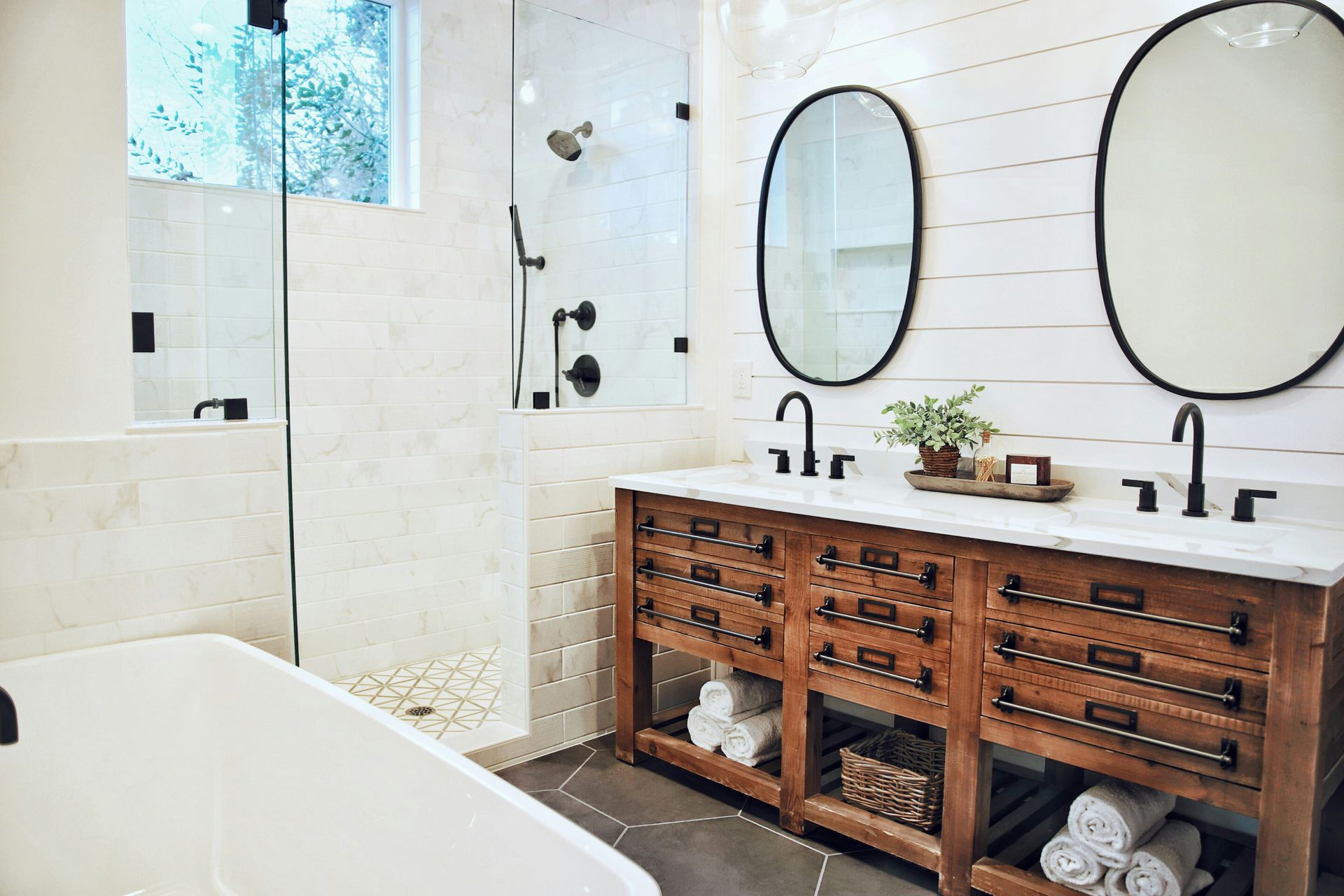 Bright bathroom with white tile, double oval mirrors, and a rustic wood vanity