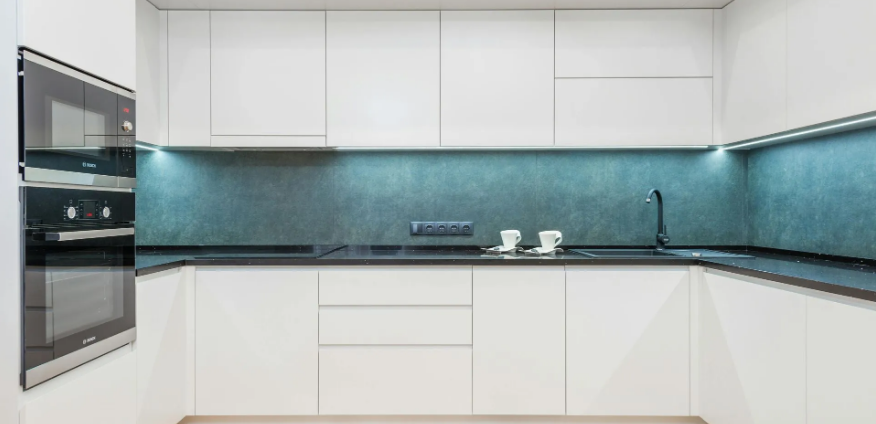 Modern white kitchen with teal backsplash, built-in oven, and black countertop