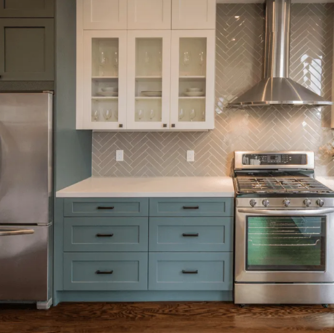 Modern kitchen with blue lower cabinets, white upper cabinets, stainless steel appliances, and tiled backsplash