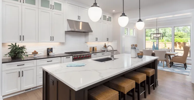Bright modern kitchen with white cabinets, marble island, pendant lights, and dining area beyond.