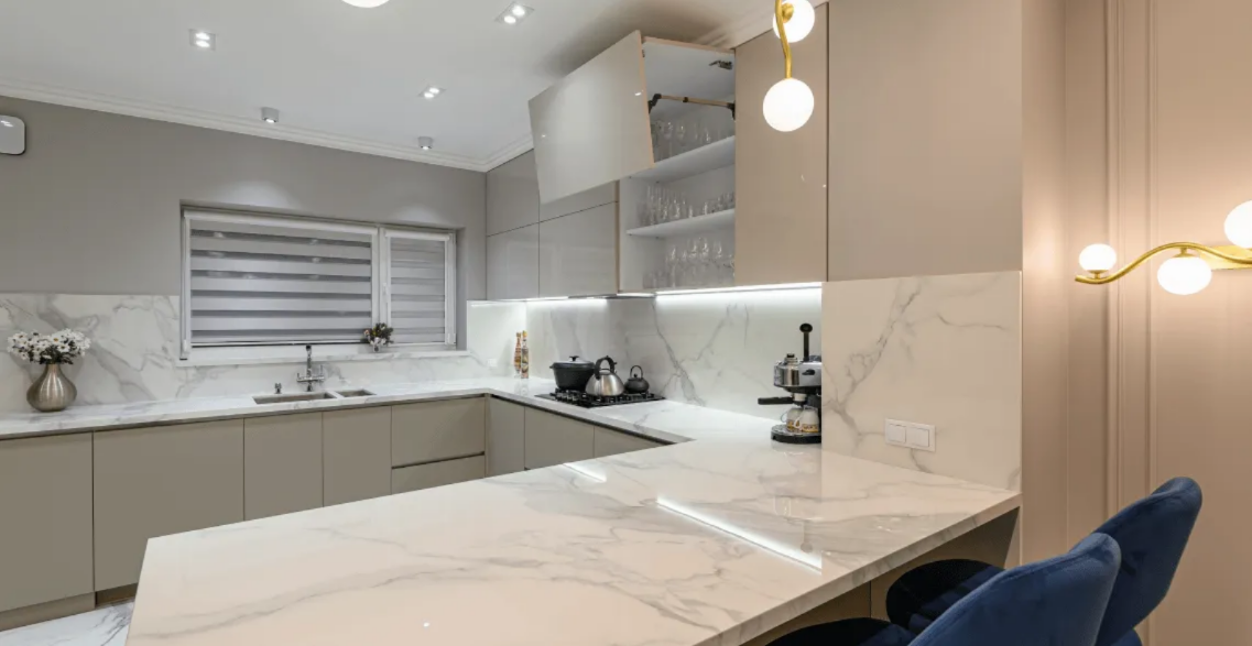 Modern white kitchen with marble island, gray cabinets, and blue bar stools under pendant lights