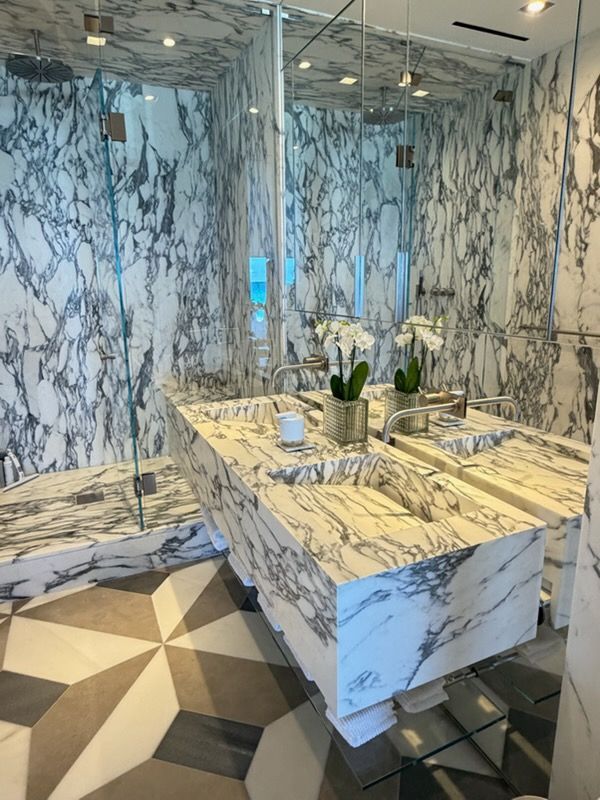 Marble-tiled bathroom with large mirror, double sink vanity, and geometric floor pattern