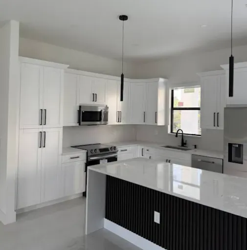 Bright modern white kitchen with island, black pendant lights, stainless appliances, and gray floor.