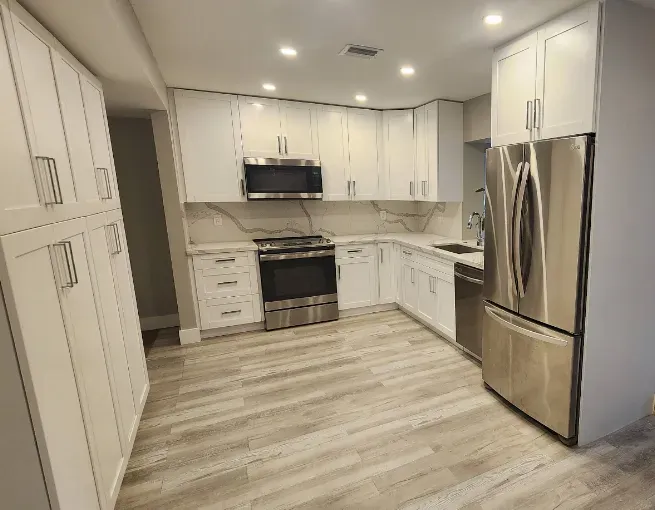 Bright modern kitchen with white cabinets, stainless steel appliances, and light wood flooring