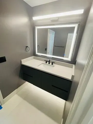 Modern bathroom vanity with a white sink, black cabinets, and backlit mirror in a gray room