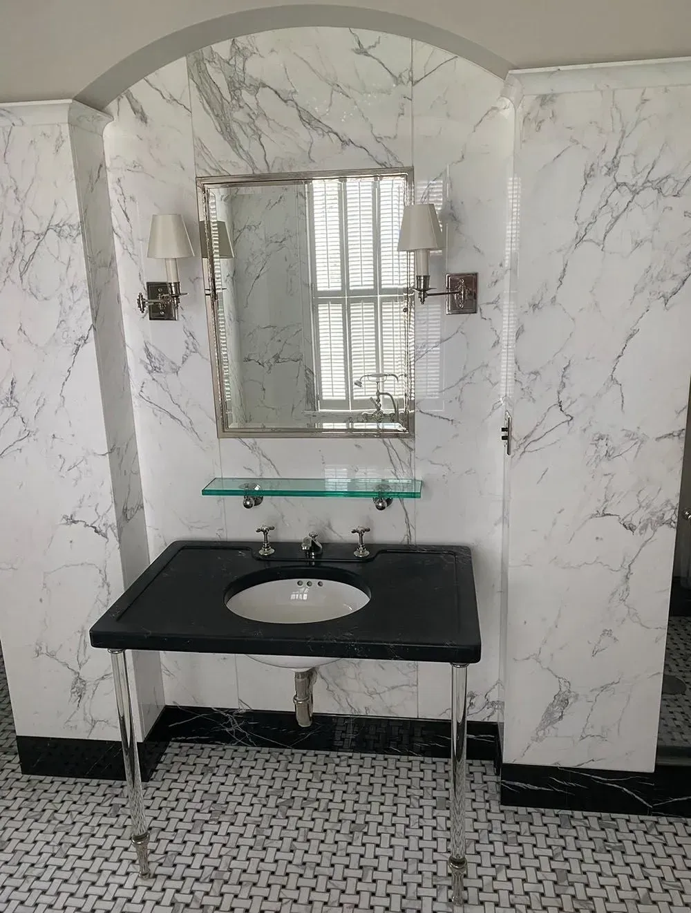 Marble-tiled bathroom vanity with black sink counter, mirror, and patterned floor.