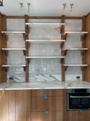 Built-in kitchen wall with white shelves, wood trim, marble backsplash, and lower cabinets with oven.