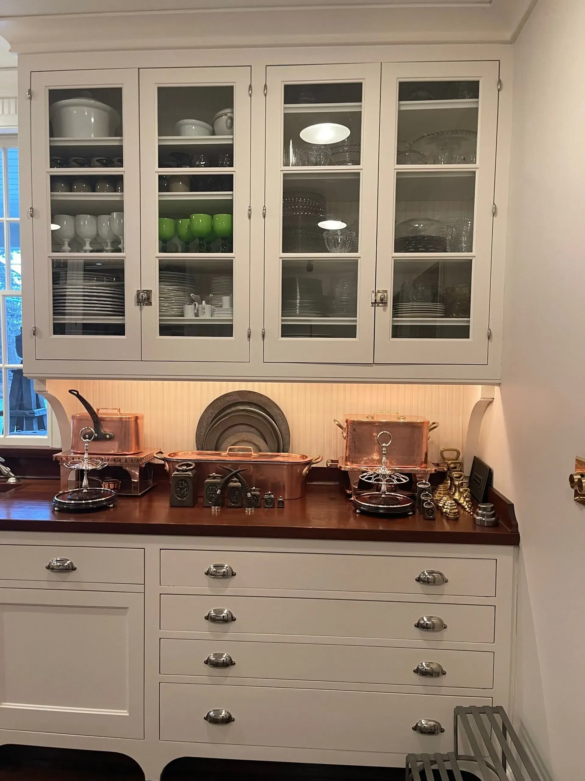 White kitchen cabinets with glass doors, copper cookware, and a dark countertop above drawers.