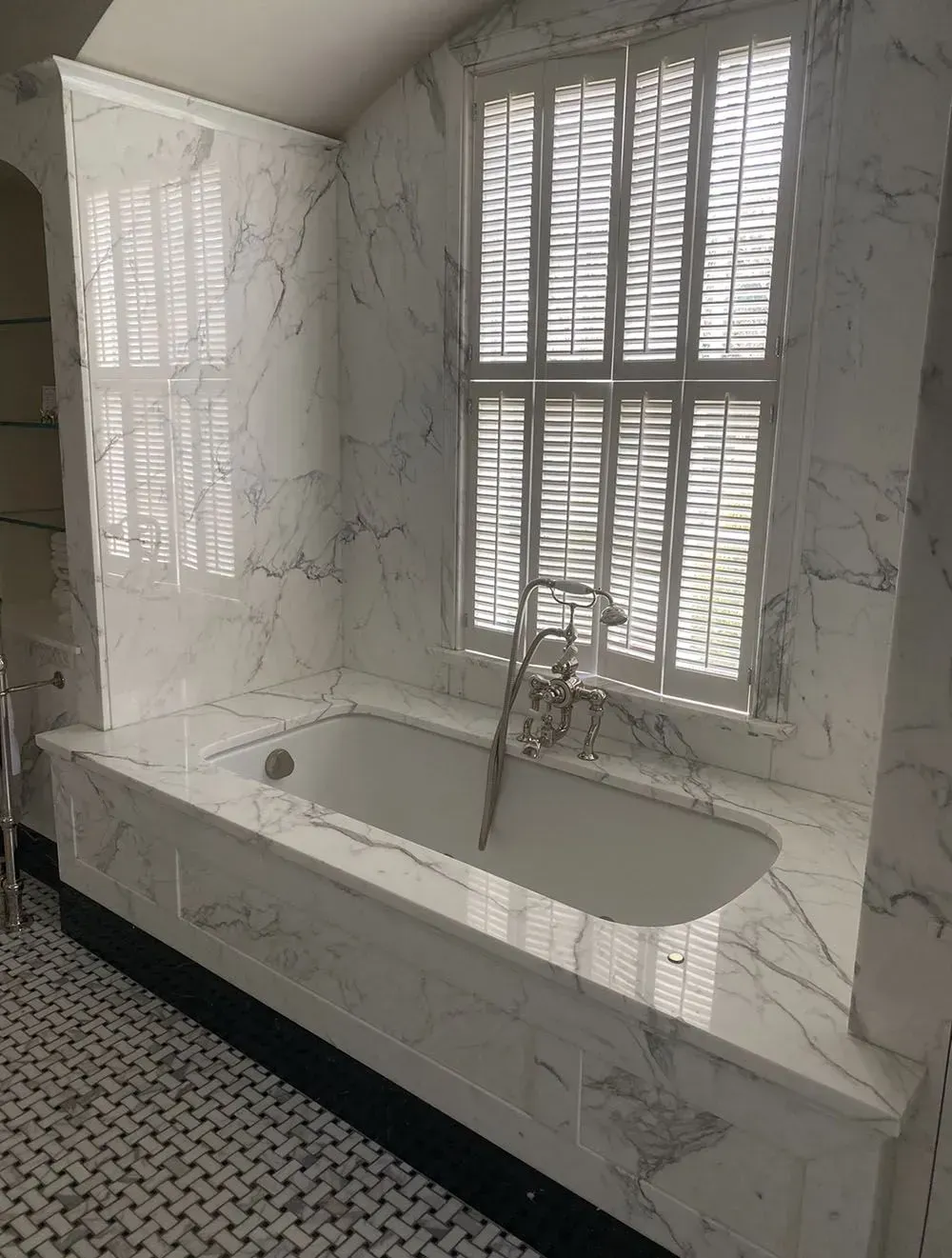 Marble bathroom with a freestanding tub, black-and-white floor tile, and window shutters