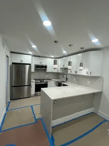 Bright white modern kitchen under renovation with stainless steel fridge, island, and blue tape on the floor