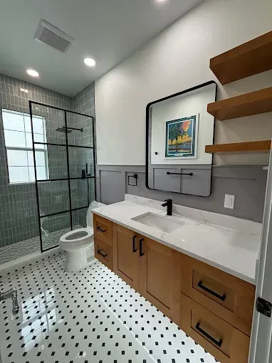 Modern bathroom with glass shower, toilet, floating vanity, black-and-white tile, and open wood shelves