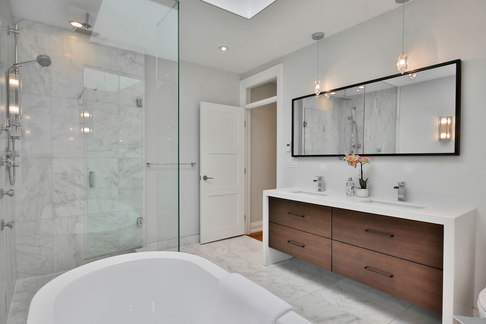 Bright modern bathroom with glass shower, freestanding tub, and wood vanity beneath a large mirror