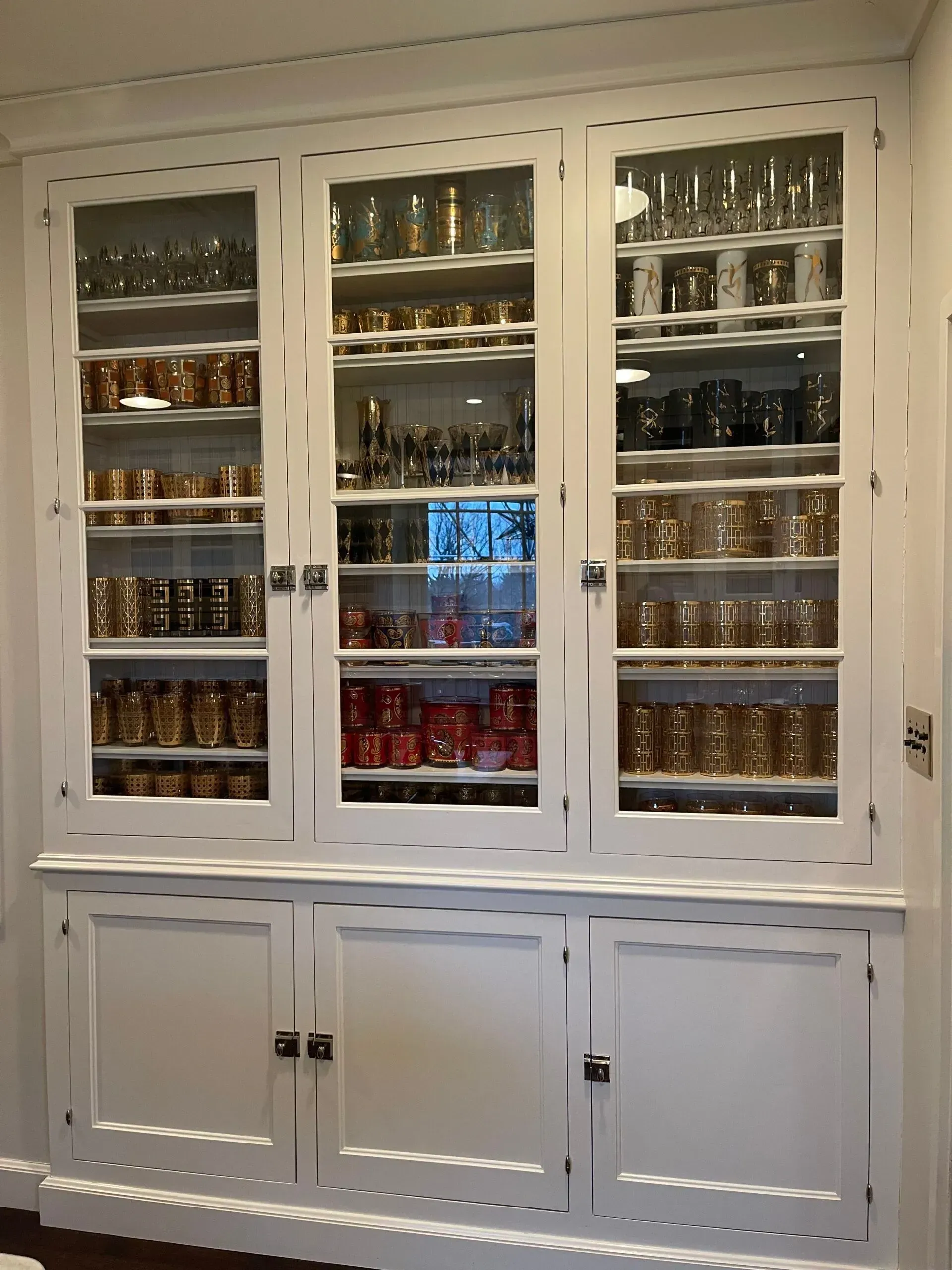 White built-in cabinet with glass doors, filled with rows of jars and glasses, above closed storage cupboards