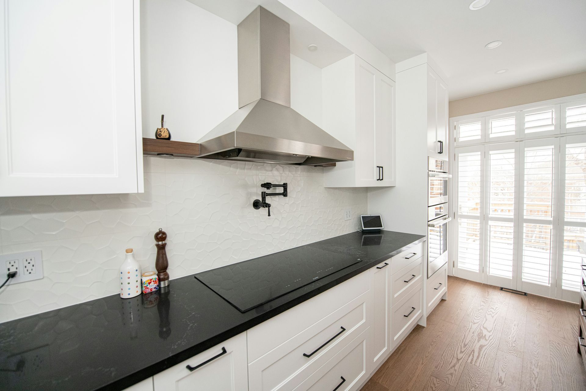 Bright modern kitchen with white cabinets, black countertops, stainless range hood, and glass doors to a patio