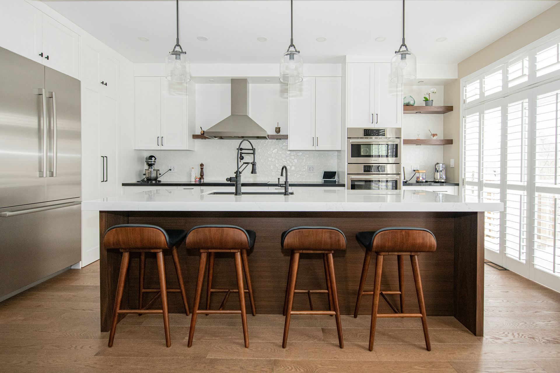 Modern white kitchen with stainless steel appliances, dark island, and four wooden stools