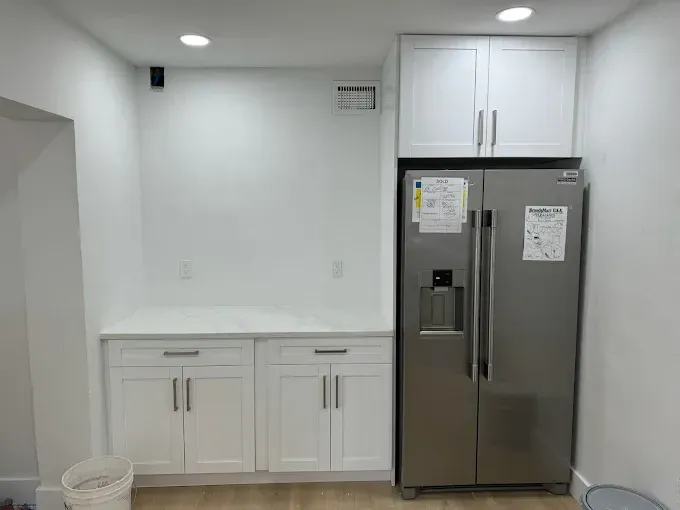 Empty modern kitchen nook with white cabinets, stainless steel fridge, and light gray walls