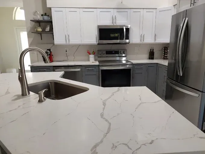 Modern kitchen with white cabinets, stainless steel appliances, and a marble island countertop.