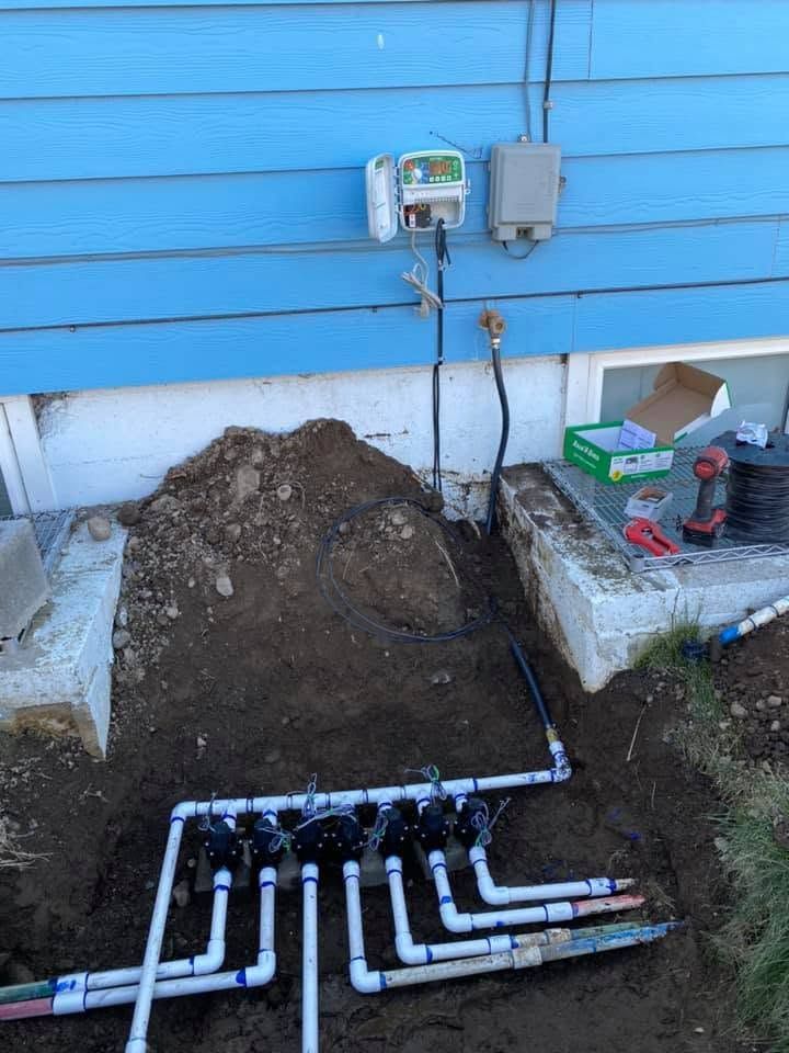 Backyard utility trench with exposed white pipes and dirt beside a blue house wall
