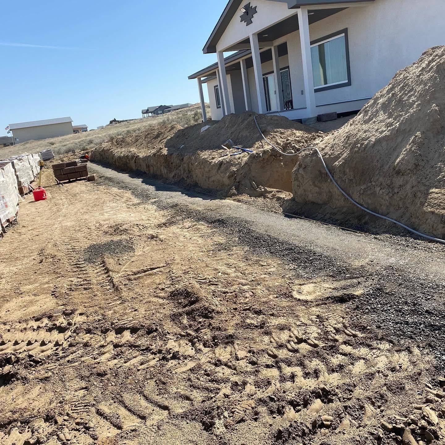 Construction trench beside a house with dirt piles and a gravel path under a clear blue sky