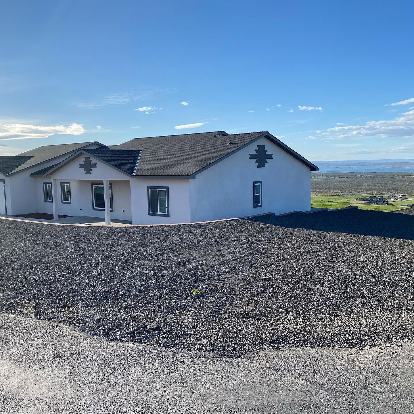 White house with dark roof on a gravel lot under a clear blue sky, overlooking a distant valley