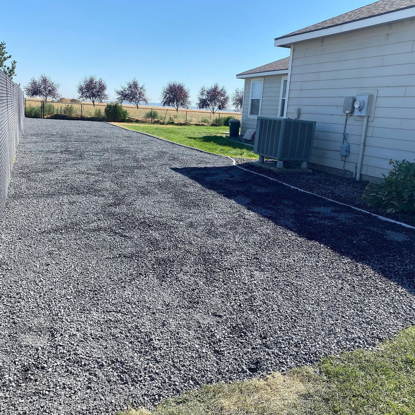 Gravel driveway beside a white house under a clear blue sky.