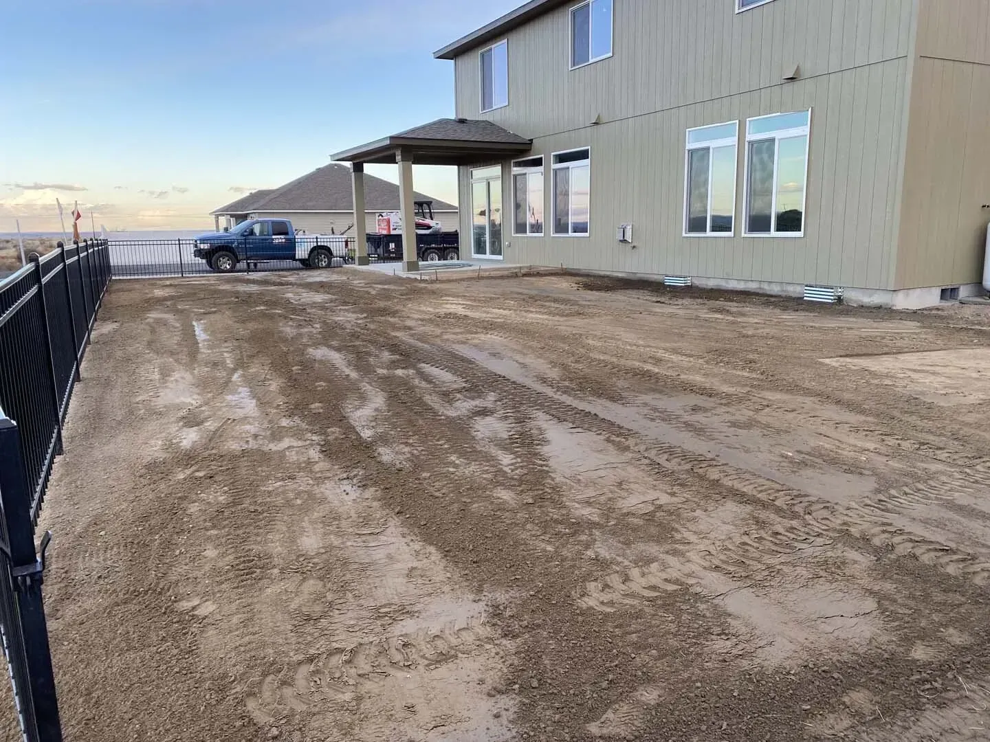 Muddy driveway beside a beige house with a covered porch and parked truck near the waterfront.
